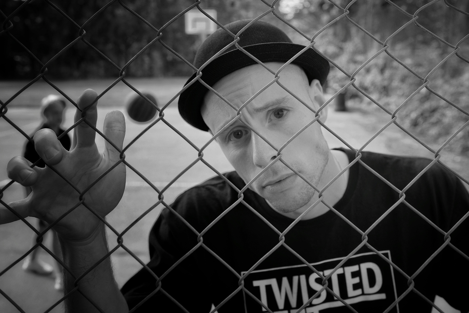 portrait of a man in a twisted t shirt behind a wire fence.